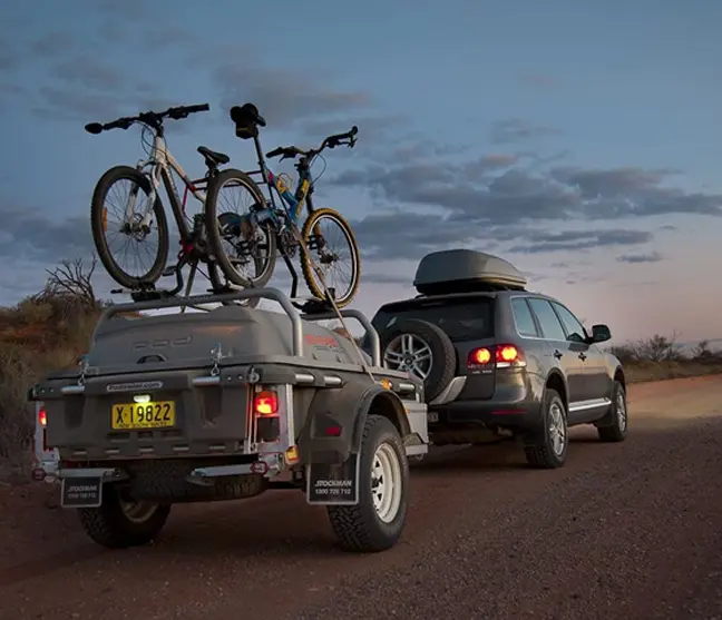 A trailer with two bikes on it and a car behind.