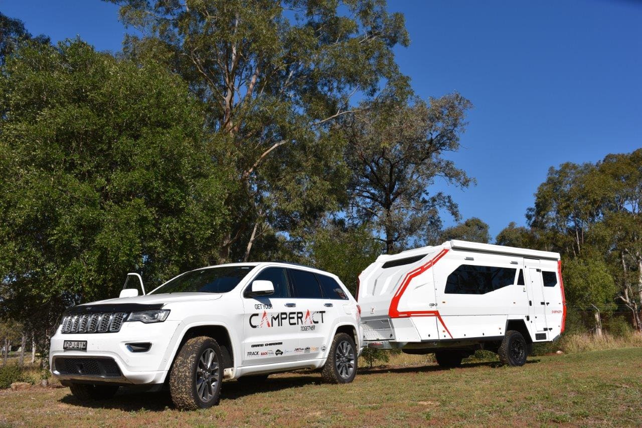 A white jeep and trailer are parked in the grass.