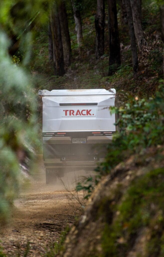 A white truck driving down the road in the woods.