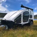 A white trailer with a black and green trim parked in the grass.