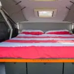 A bed with red and white sheets in the back of an rv.