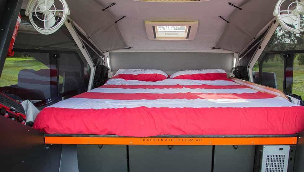 A bed with red and white sheets in the back of an rv.