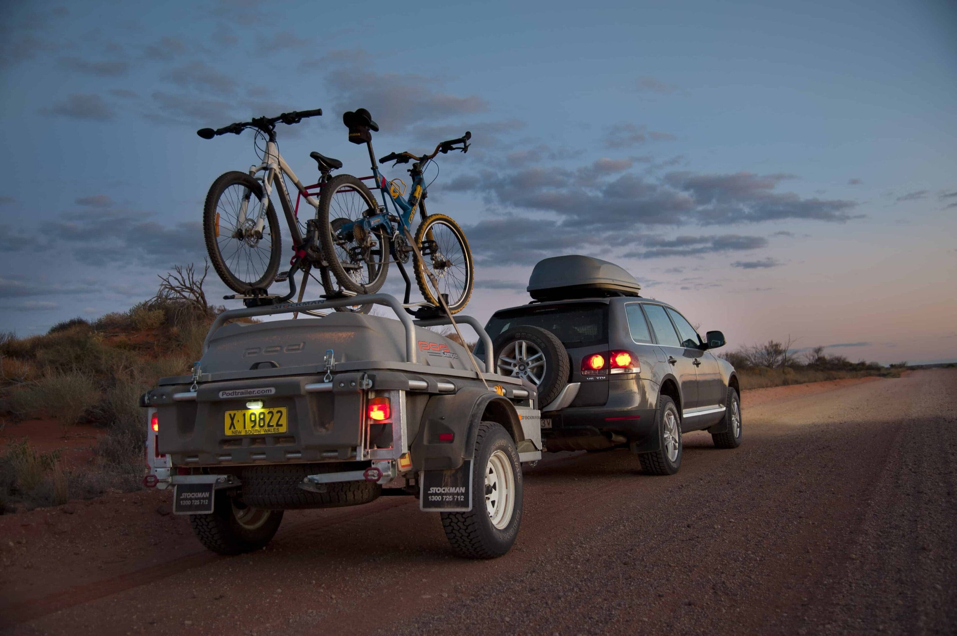 A trailer with two bikes on it and the back of a car.