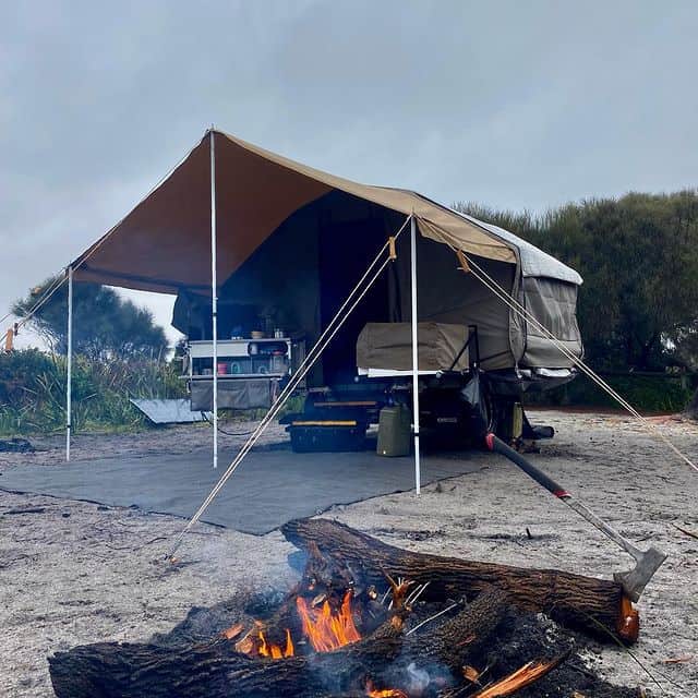 A tent is pitched on the ground near some fire.