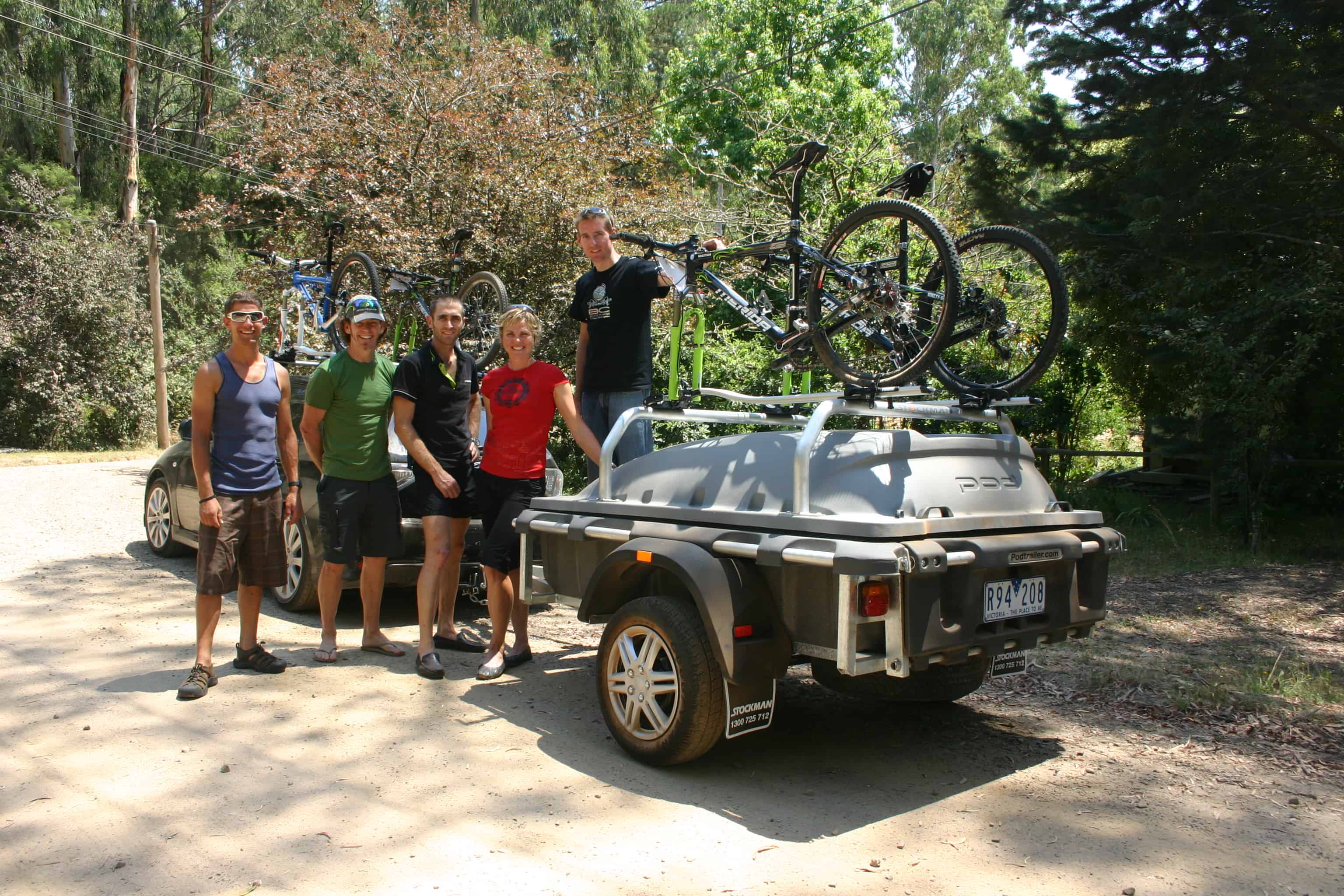 A group of people standing around a trailer with bicycles on it.